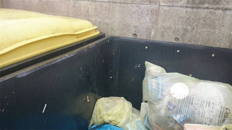 Ein schwarzer Mülleimer voller Abfall und einem gelben Deckel.