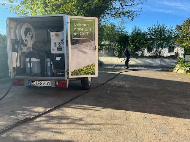 Ein Mann reinigt eine Einfahrt mit einer Maschine auf der Ladefläche eines Anhängers.