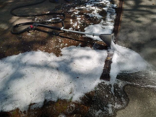 Eine Person reinigt eine Bank mit einem Hochdruckreiniger.