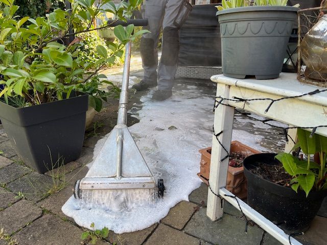 Eine Person reinigt eine Terrasse mit einem Besen.