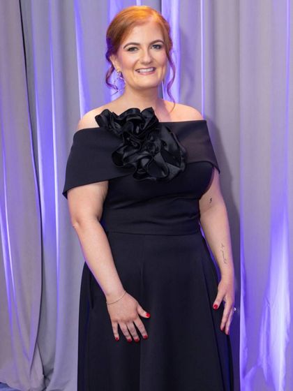 A woman with red hair is wearing a green jacket and a gold necklace.