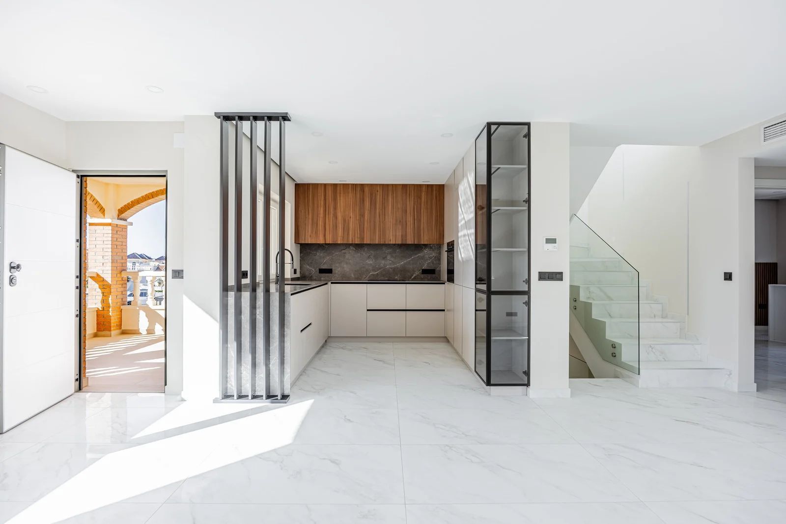 Modern kitchen with wood and white cabinets, marble floors, and a staircase. Bright and spacious.
