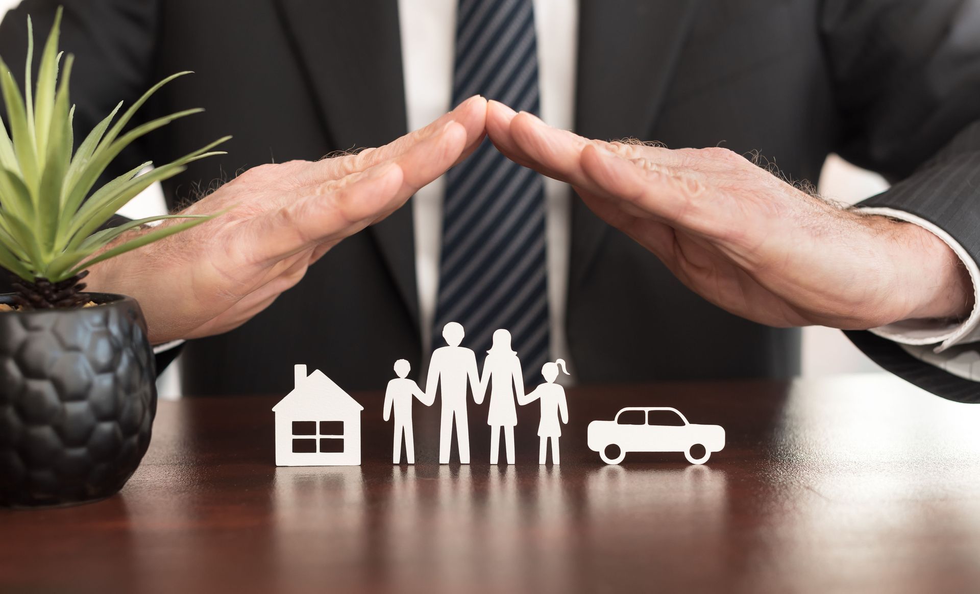 a man in a suit and tie covers a family a house and a car with his hands
