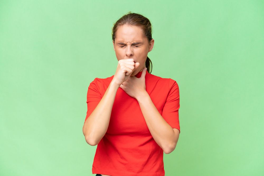 a woman in a red shirt is coughing into her hand