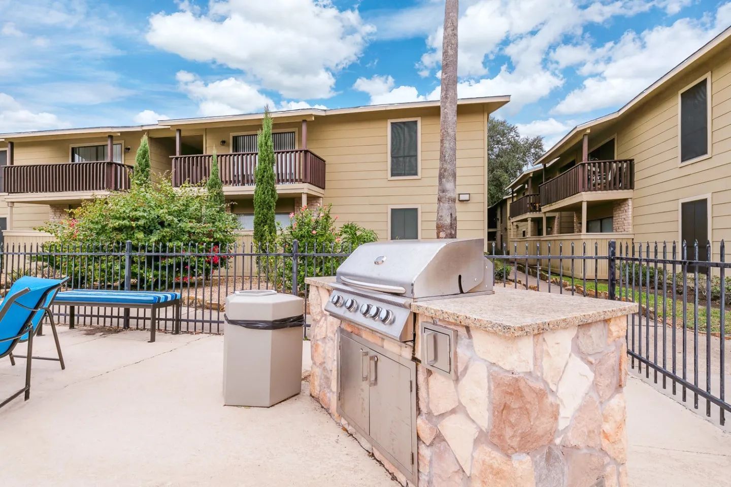 a fenced in area with a grill and a trash can