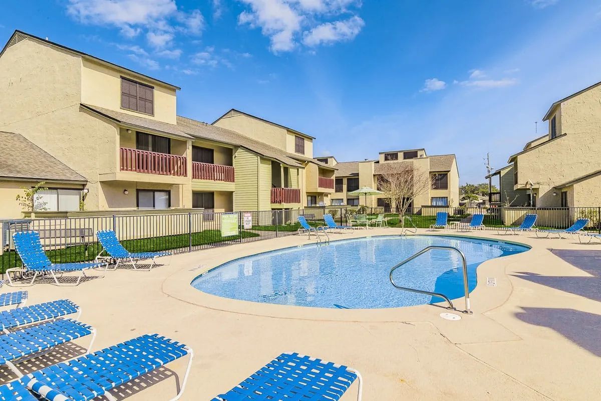 a swimming pool surrounded by chairs and umbrellas in front of a building