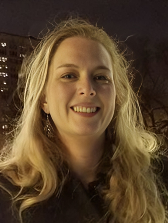 A woman with long blonde hair is smiling in front of a christmas tree