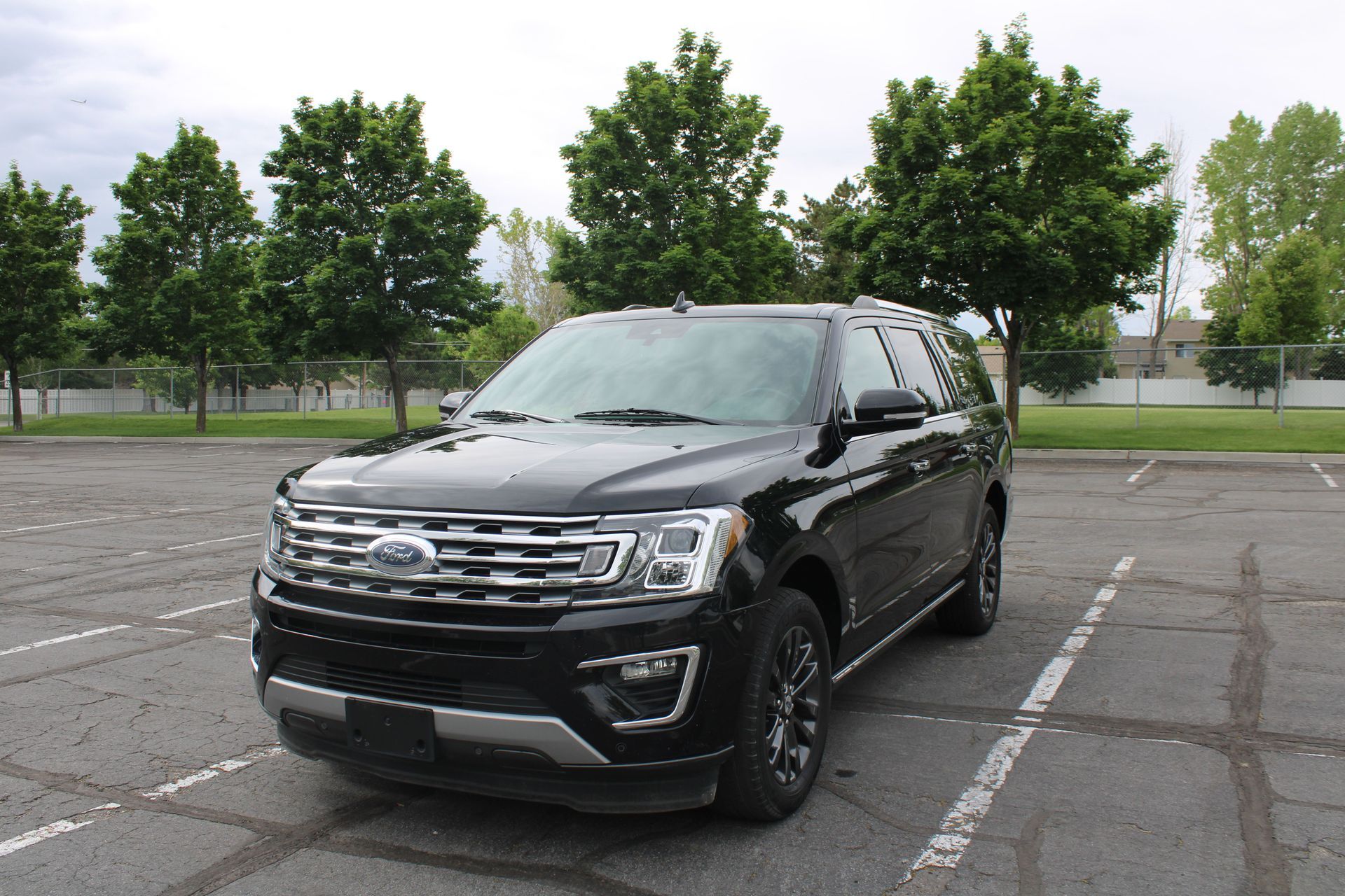 Black Ford Expedition SUV parked in a parking lot in front of trees.
