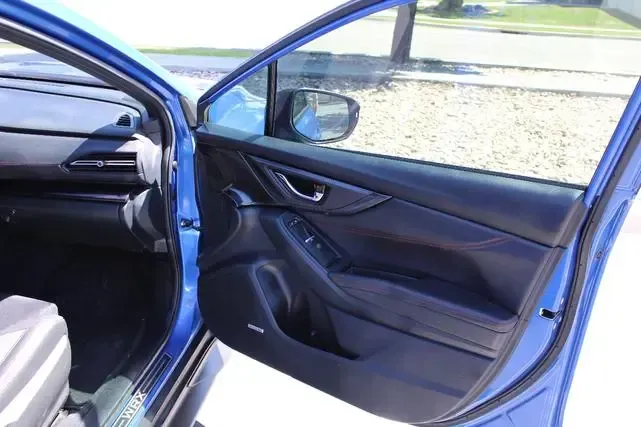 A blue car with the door open is parked on the side of the road.