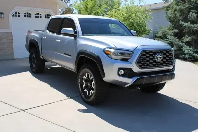 A silver toyota tacoma is parked in a driveway in front of a garage.