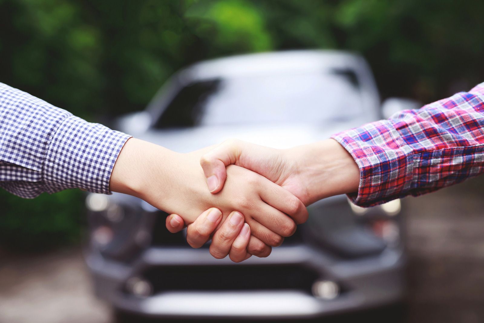 Two people are shaking hands in front of a car.