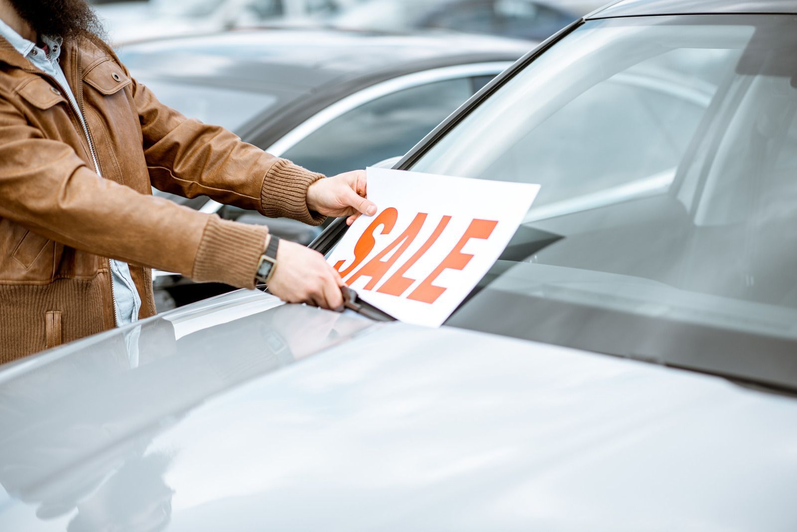 A man is holding a sale sign on the windshield of a car.