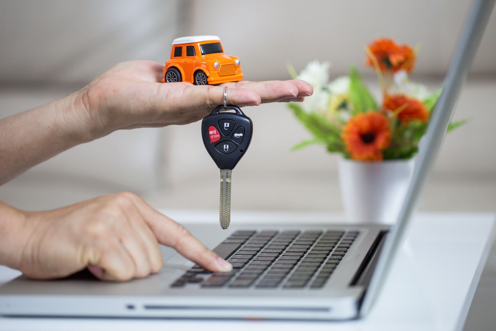 A person is holding a toy car and a car key in front of a laptop computer.