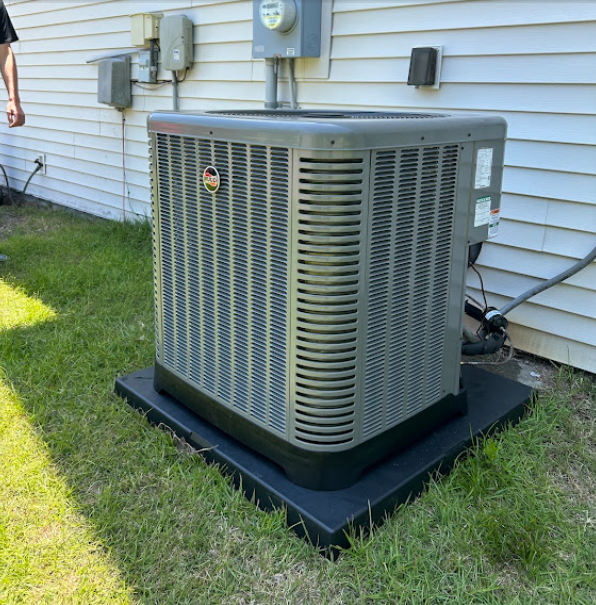A large air conditioner is sitting in the grass in front of a house.