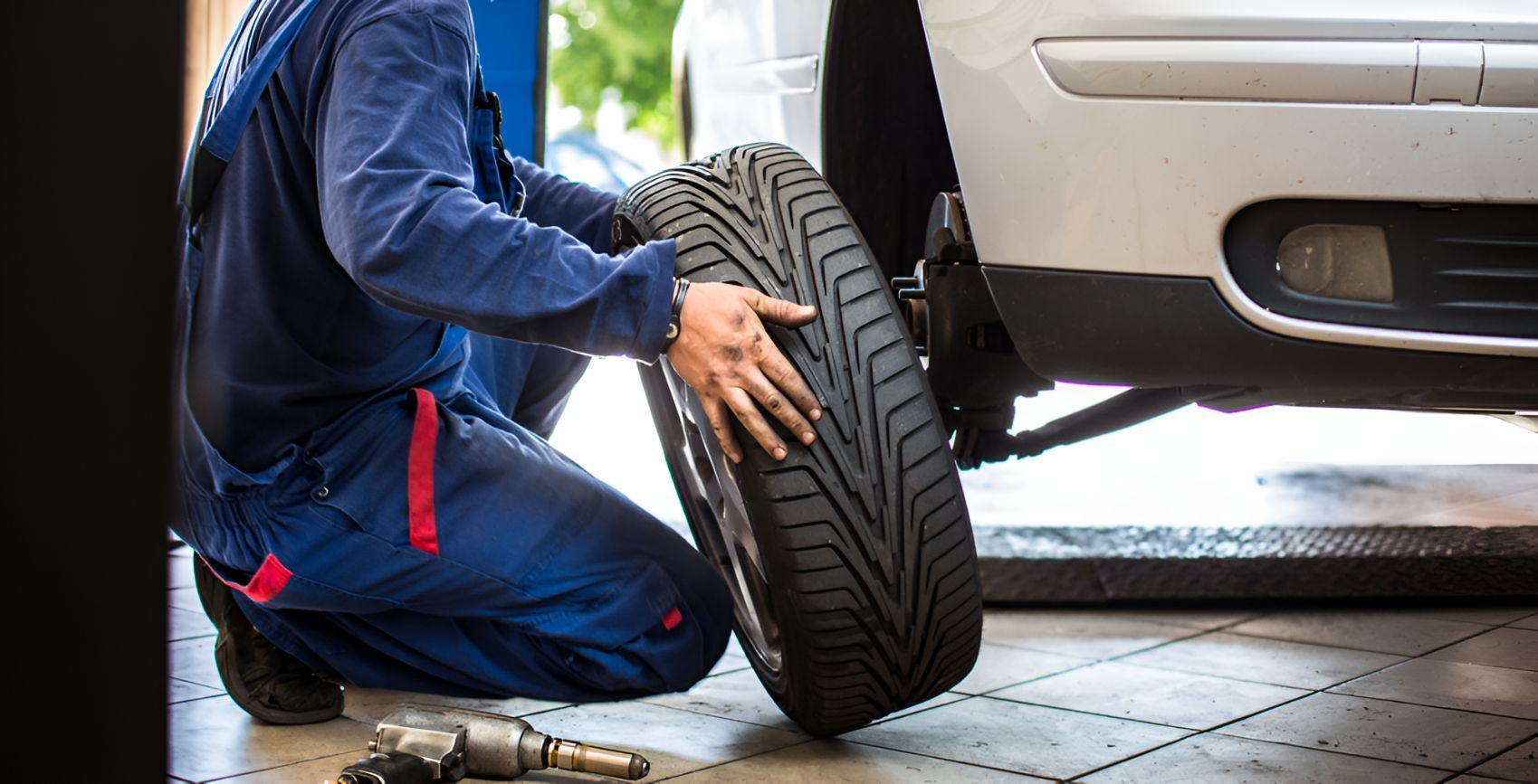 A Mechanic is Kneeling Down to Change a Tire on a Car — Empire Automotive In Portsmith, QLD