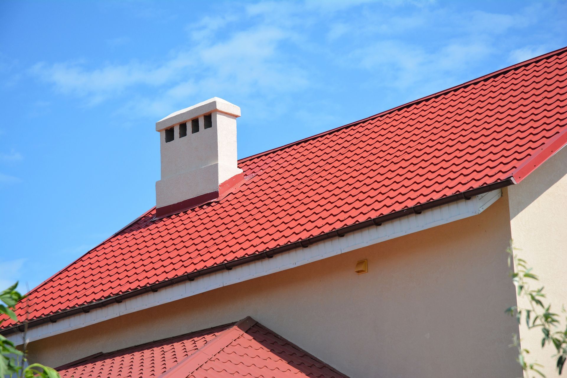 Tetto di tegole rosse con un camino beige sullo sfondo del cielo azzurro.