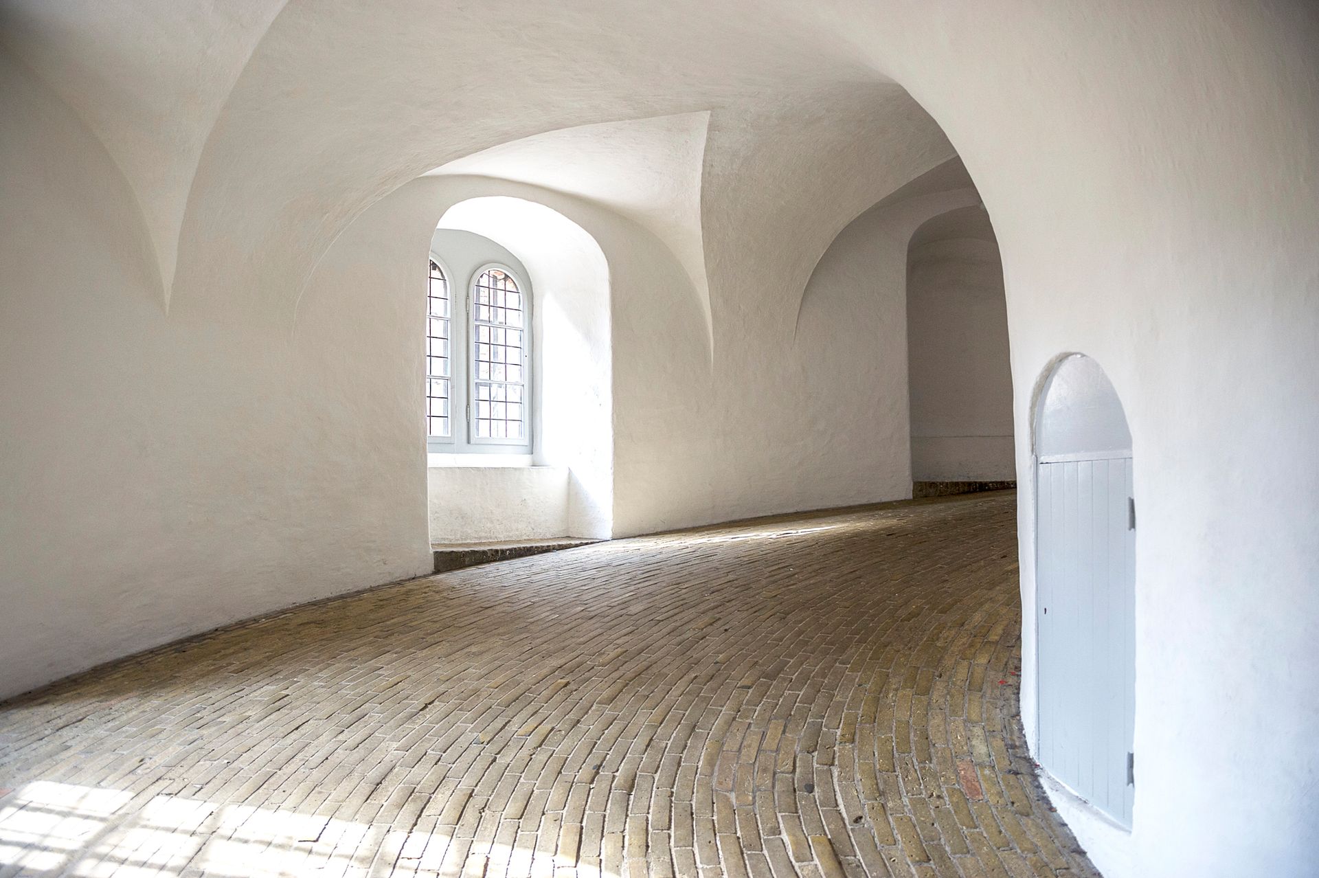 Corridoio bianco ad arco con pavimento in ciottoli e una finestra.