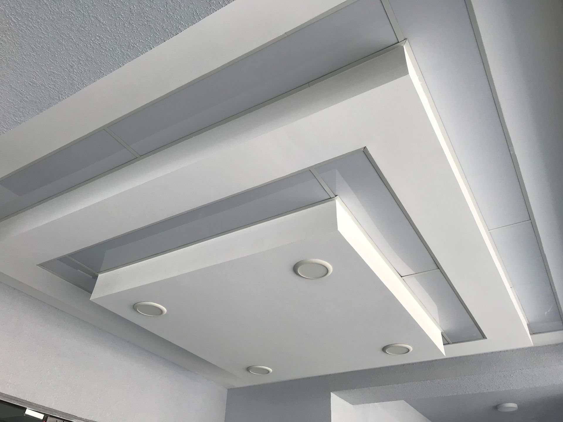 Soffitto bianco, a strati, dal design geometrico con illuminazione da incasso.