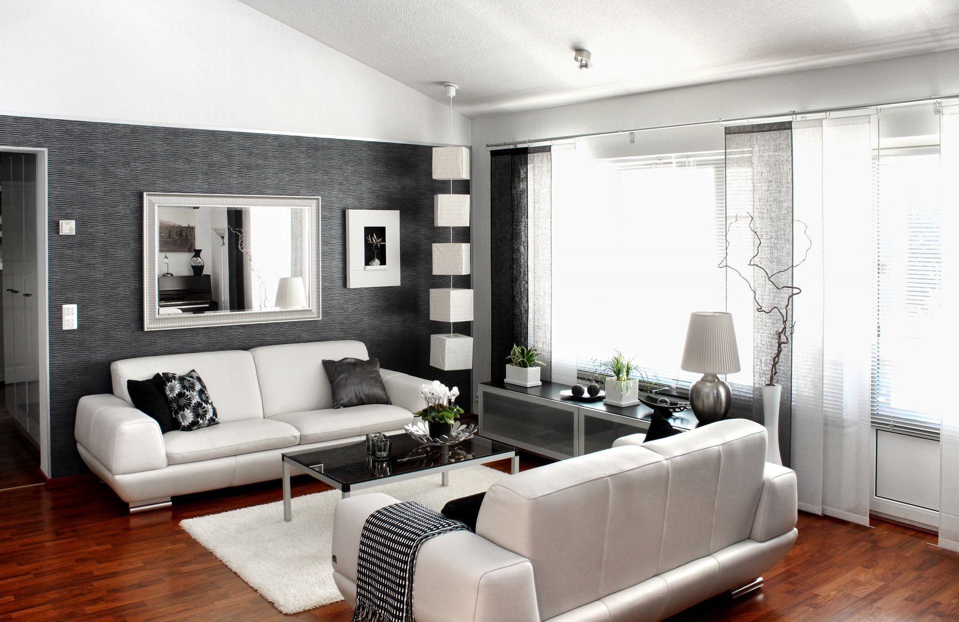 Soggiorno moderno con divani bianchi, parete scura, specchio e ampie finestre.