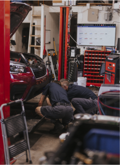 Technician working under red car in garage | Andrew's Automotive Repair