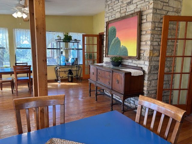 A dining room with a blue table, wooden chairs, a stone fireplace wall, a buffet sideboard, and large windows.