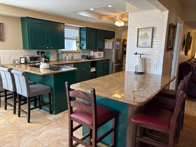 A kitchen with dark green cabinets, granite countertops, two gray stools, and a center island with two burgundy chairs.
