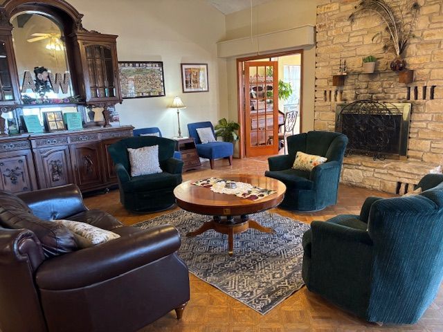 A cozy living room with a stone fireplace, dark armchairs, a leather sofa, and a circular wooden coffee table on a rug.