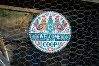A sign that says welcome to our coop is on a chicken wire fence.