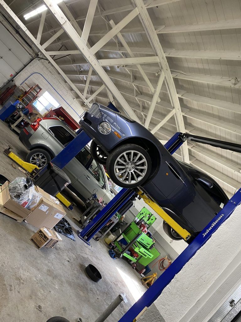 A blue luxury car is raised on a lift in a repair shop, another car in background. | Loyola Service