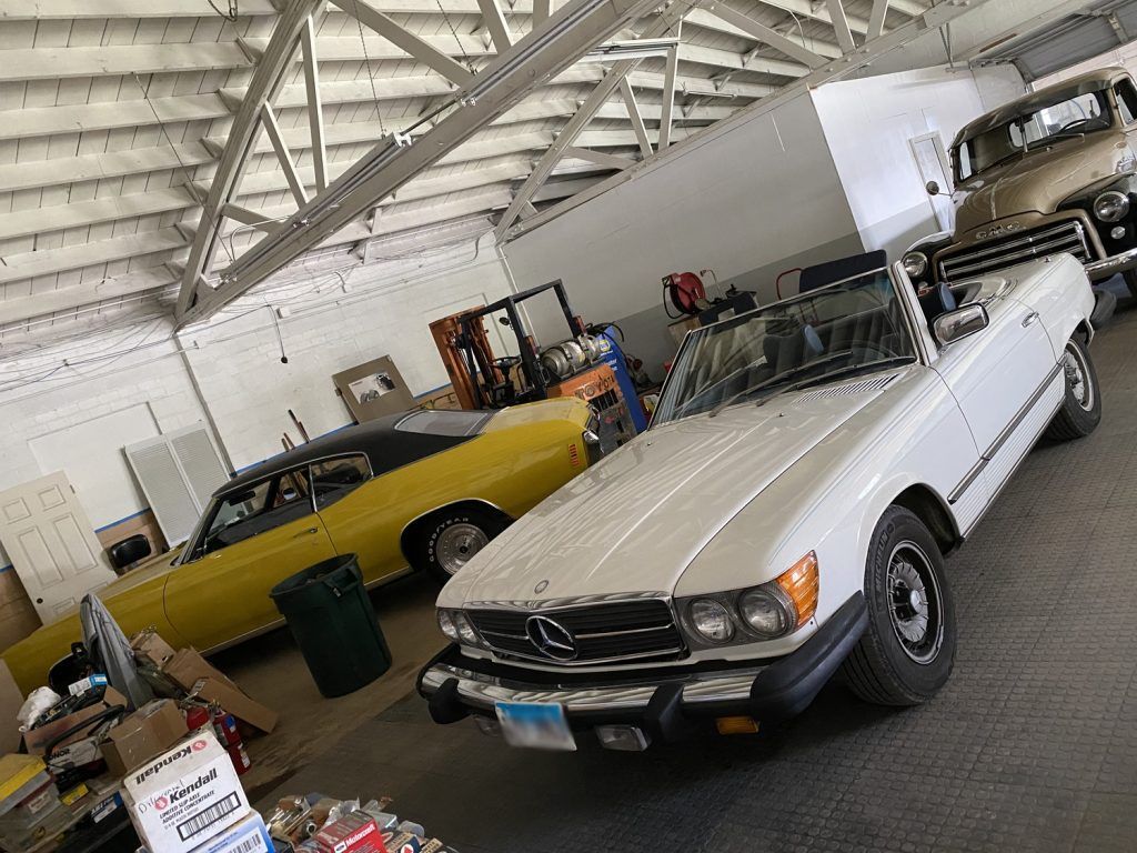 White convertible Mercedes and yellow classic car in a garage. | Loyola Service