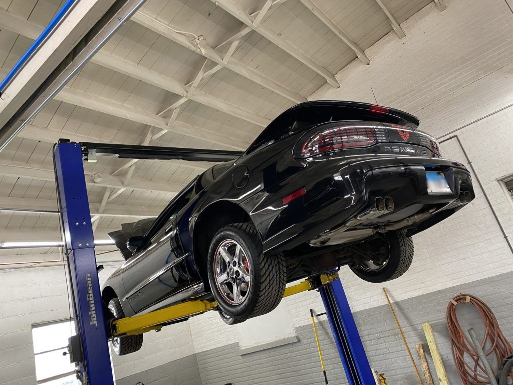 Black car on a lift in a garage, tires visible, undercarriage exposed, white ceiling, Illinois license plate. | Loyola Service