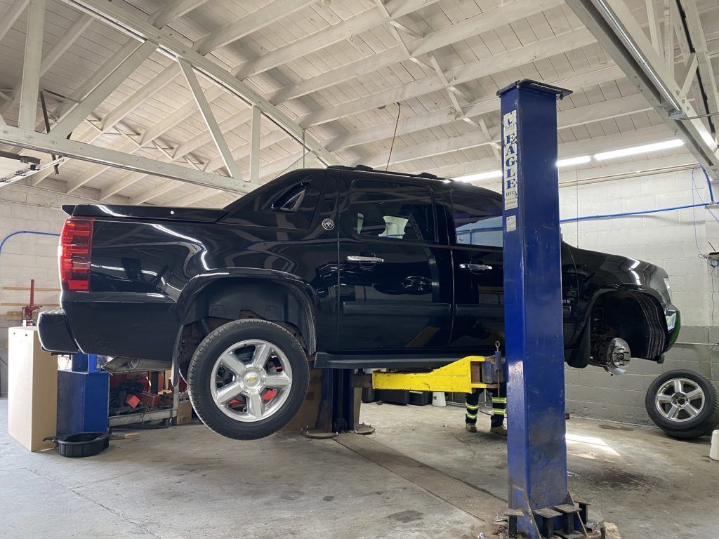 Black truck on a lift in a repair shop. The front tire is missing. | Loyola Service