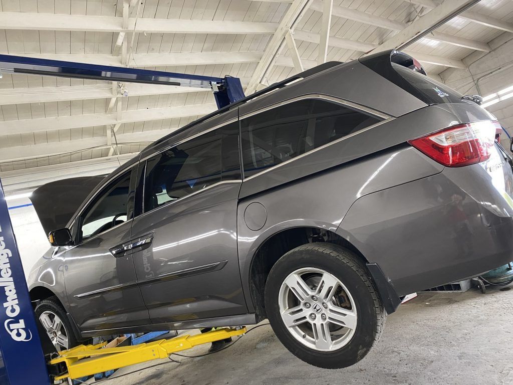 Gray minivan on a lift in a mechanic's shop, hood open. | Loyola Service