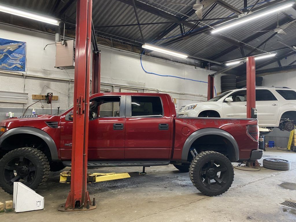 Red truck on a lift in an auto repair shop; another vehicle on a lift in the background. | Loyola Service