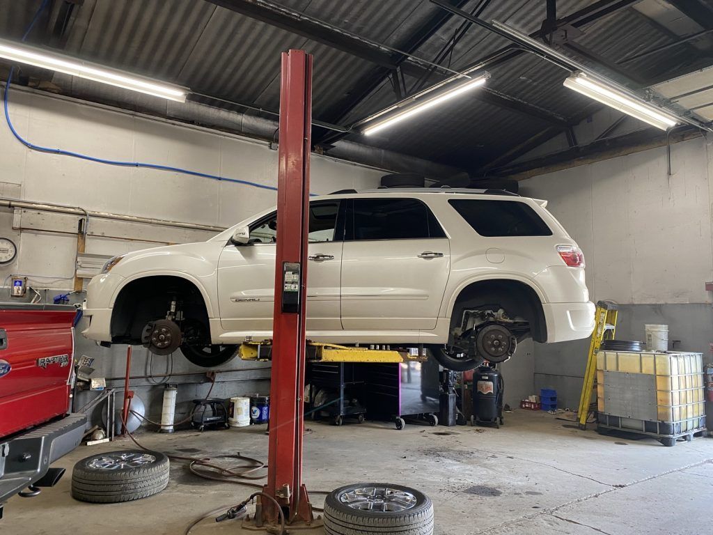 White SUV on a lift in a garage; tires removed, mechanic likely working on brakes. | Loyola Service