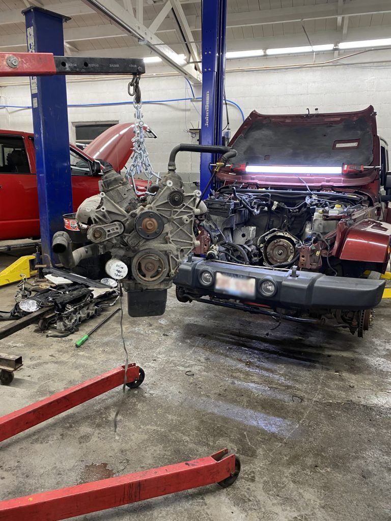 Jeep with engine removed at a mechanic shop. Engine suspended, hood up, with tools and parts scattered. | Loyola Service