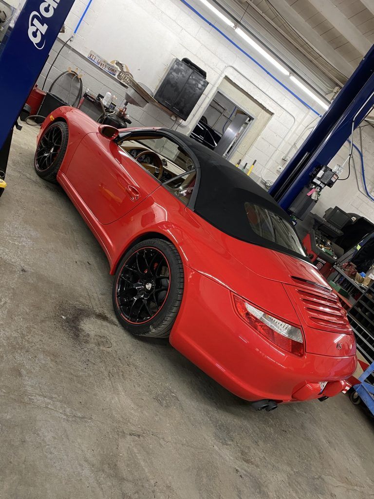 Red convertible sports car in a garage, black wheels and roof, angled shot. | Loyola Service