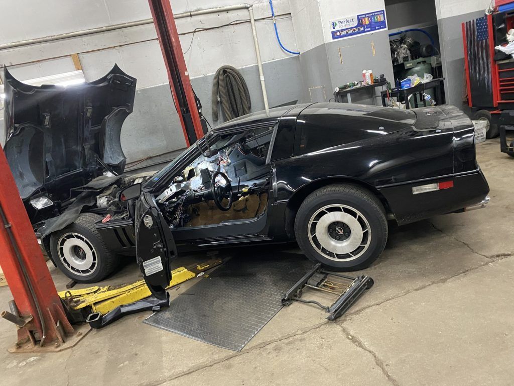 Black classic car in a garage with hood up, door open, and seat frame removed. | Loyola Service