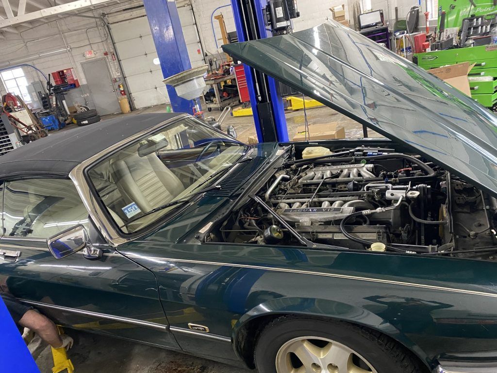Green Jaguar convertible with open hood in a repair shop, engine visible. | Loyola Service