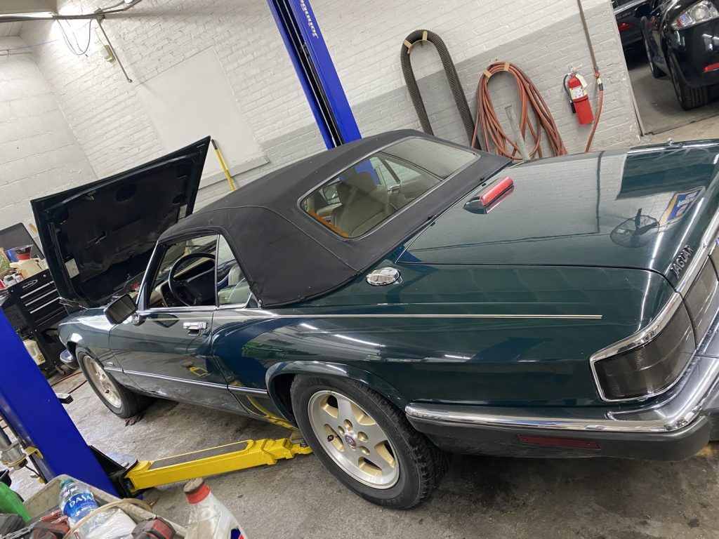 Green Jaguar convertible on a lift in a repair shop, hood open. | Loyola Service