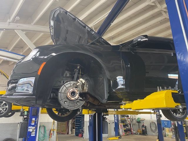 Black car on a lift in a repair shop with hood open, front wheel removed, and tools visible. | Loyola Service