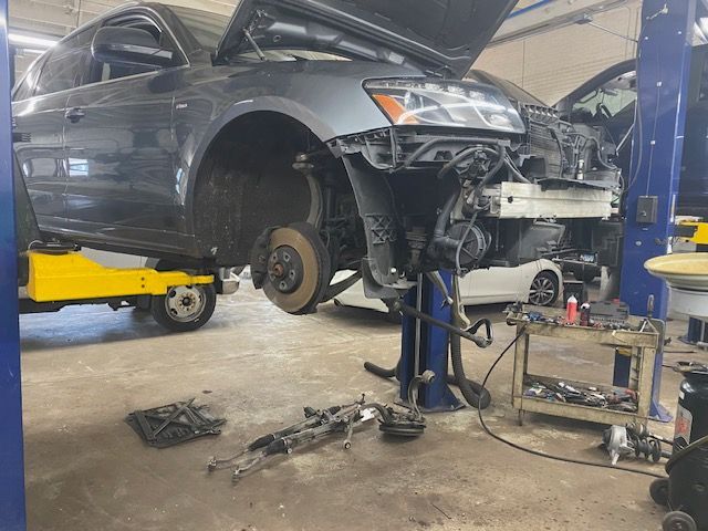 Car being repaired in a shop, front end disassembled, raised on a lift. Grey vehicle, tools and parts visible. | Loyola Service