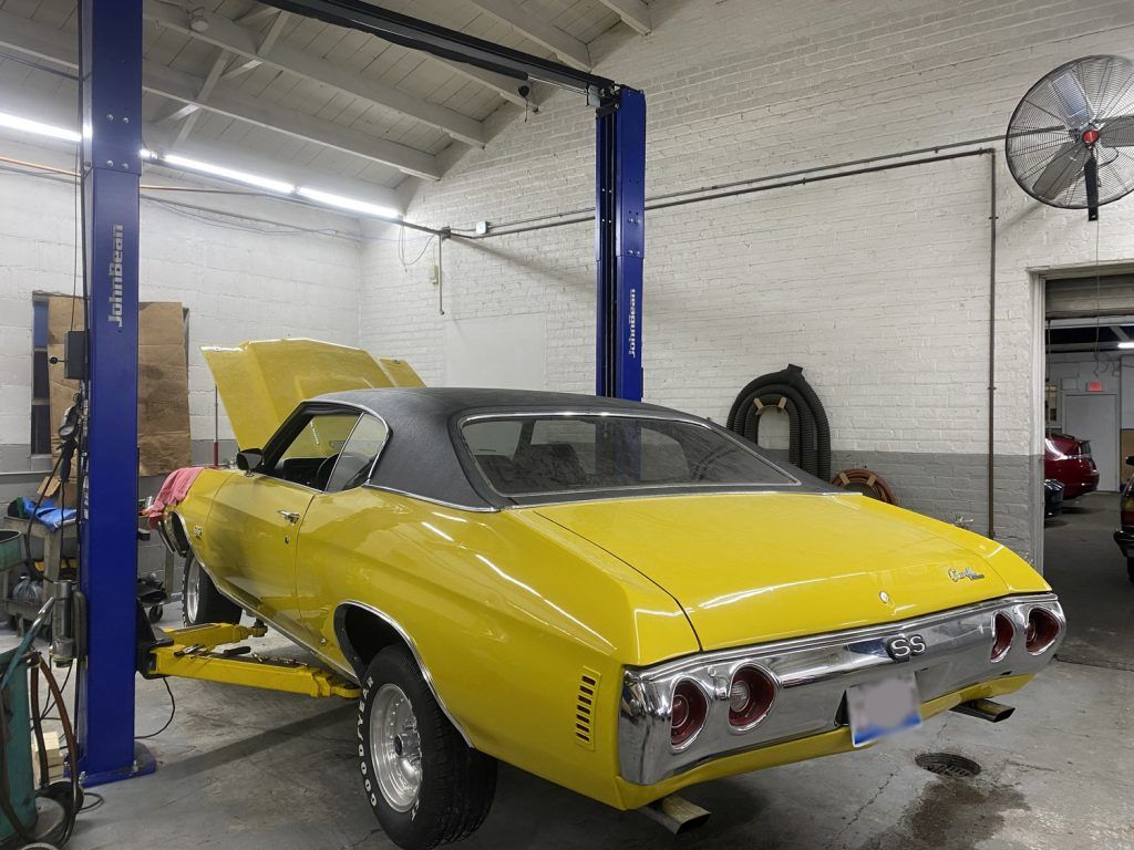 Yellow classic car on a lift in a garage. Hood open. | Loyola Service