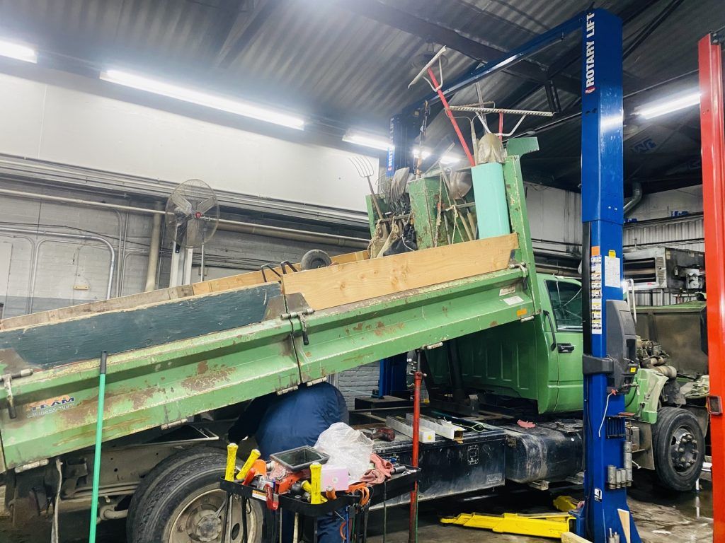 A green dump truck, raised by a lift in a garage. | Loyola Service