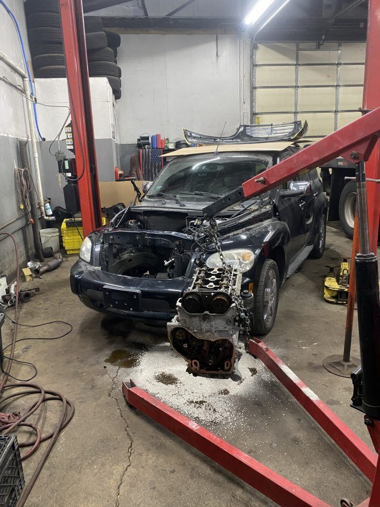 Car with engine removed in auto repair shop. Black vehicle under lift. Red engine crane. | Loyola Service