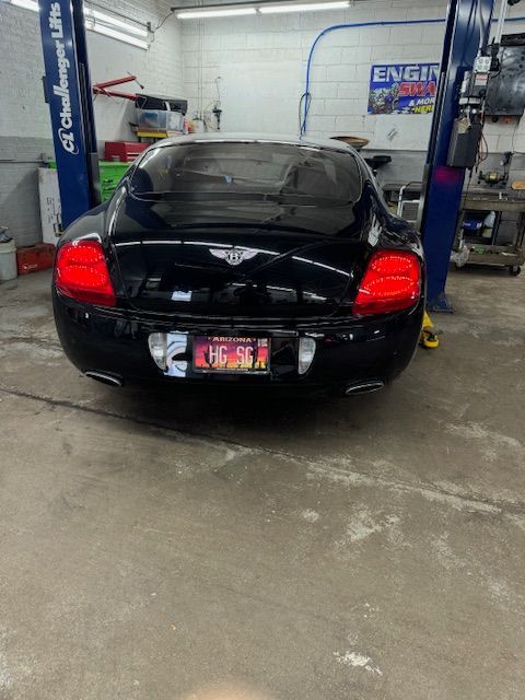 Black Bentley Continental in a garage, rear view. Tail lights illuminated, license plate visible. | Loyola Service