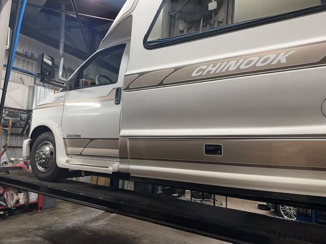 White and tan Chinook RV on a lift inside a garage. Door is open. | Loyola Service
