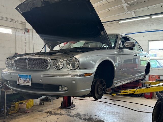 Silver Jaguar sedan on a lift with the hood open, inside a repair shop. | Loyola Service