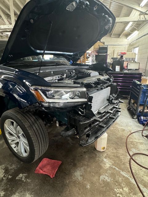 Dark blue car with open hood, front end damage, in a repair shop. | Loyola Service