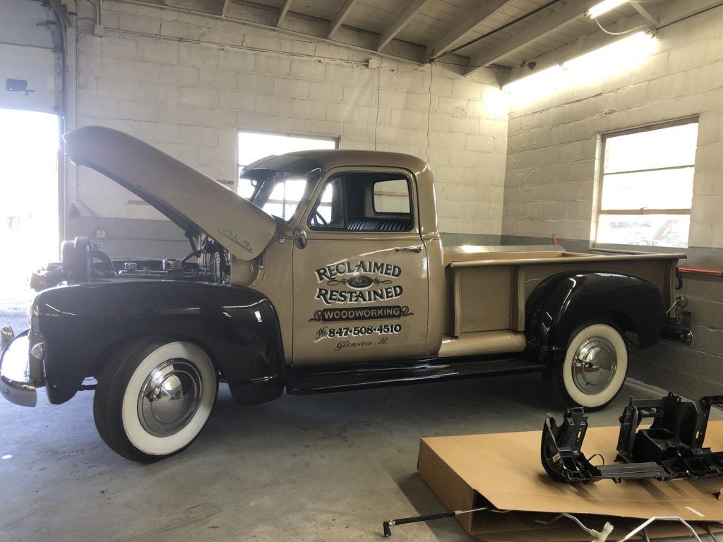 Tan and black vintage pickup truck in a garage with hood open, white-walled tires, signage. | Loyola Service